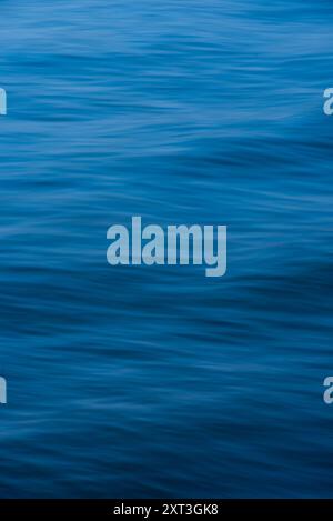 An artistic close-up photograph of the sea's surface, featuring smooth, flowing textures in various shades of blue, epitomizing tranquility and the fl Stock Photo