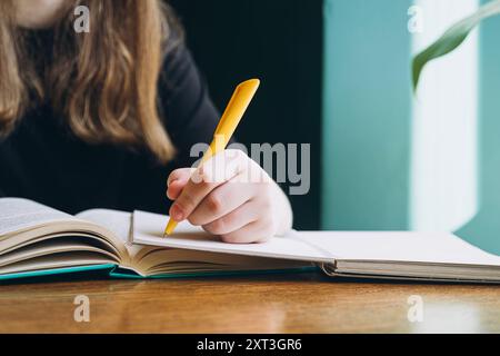 Cropped unrecognizable female student focuses on her studies, writing in a notebook at a wooden desk, with a blurred background enhancing concentratio Stock Photo