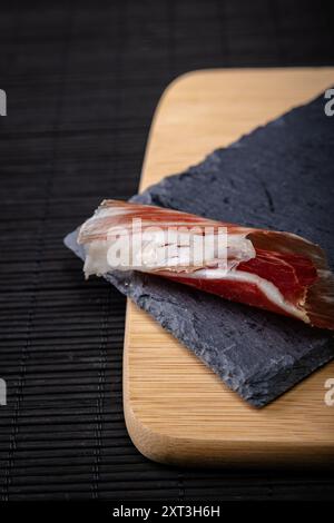 A close-up image showcasing thin slices of Serrano ham artistically placed on a slate board atop a wooden surface, exemplifying a quintessential Spani Stock Photo
