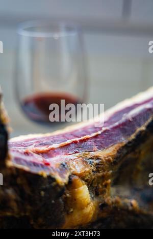 This close-up image captures a delectable piece of Cured Iberian Ham with a glass of red wine in the background The rich colors and textures highlight Stock Photo