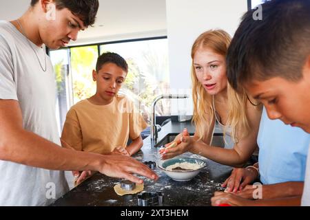 Family enjoy baking together, using cookie cutters on dough in a modern, sunny kitchen, demonstrating teamwork and family bonding Stock Photo