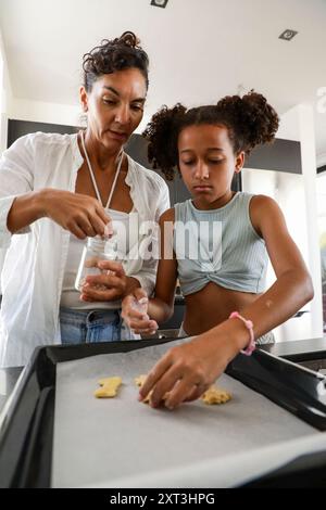 An intimate family moment in the kitchen with a mother and her daughter preparing cookies together The mother is helping her daughter sprinkle ingredi Stock Photo