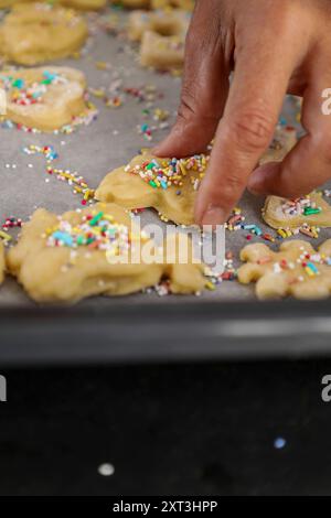 Close-up image of a hand decorating animal-shaped sugar cookies with colorful sprinkles on a baking sheet Stock Photo