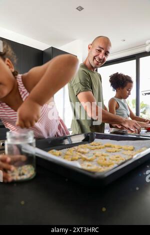 A joyful family moment as a father and his two children engage in baking cookies at home The cozy kitchen setting highlights the fun and bonding over Stock Photo