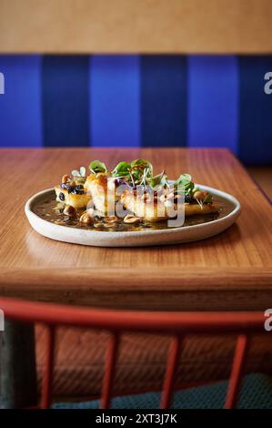 Grilled halloumi cheese served on a ceramic plate with seeds and microgreens, presented on a wooden table with a blue upholstered booth in the backgro Stock Photo