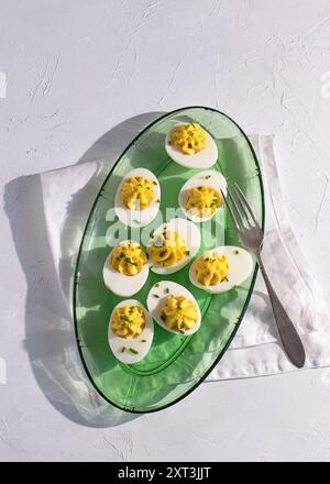Top view of classic deviled eggs served in a transparent green glass dish, highlighted by natural sunlight casting soft shadows, perfect for a gourmet Stock Photo