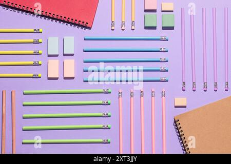 Flat lay of colorful back to school supplies with notebooks, pencils, and erasers on a purple background shot from above. Stock Photo