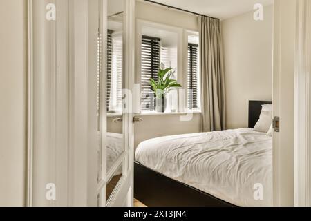 A tranquil bedroom design featuring white linens, plantation shutters, and a fresh plant by the window inviting natural light and serenity. Stock Photo