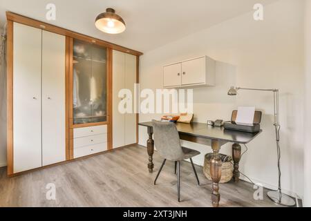 A contemporary home office featuring a dark wood desk, comfortable chair, large wardrobe, and elegant lighting. Stock Photo