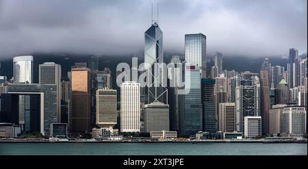 A panoramic view of the Hong Kong cityscape, featuring the iconic skyline under a blanket of dark, stormy clouds The image captures a striking contras Stock Photo