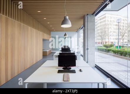 A sleek, modern office or coworking space featuring a white minimalist desk, contemporary wooden wall panels, and hanging light fixtures, with a view Stock Photo