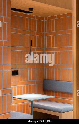 A cozy booth featuring orange brick walls and a simple pendant light The space combines natural wood accents and a grey padded bench, ideal for modern Stock Photo