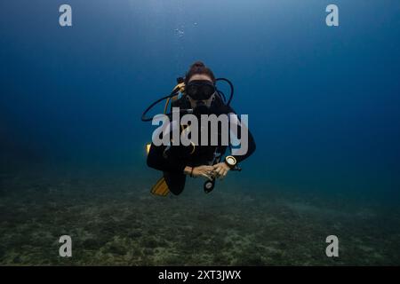 In this image, a female diver is depicted swimming underwater in a clear blue ocean environment. She is equipped with a scuba gear, including a mask, Stock Photo
