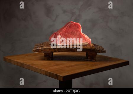 A high-quality raw tuna steak displayed on a rustic wooden cutting board, set against a dark, textured backdrop, ideal for sushi preparation themes Stock Photo