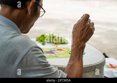 Vietnamese artisan expertly sews colorful threads into a fabric, creating a traditional embroidered textile pattern The focus is on skilled hands and Stock Photo