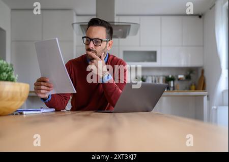 Focused male entrepreneur analyzing business report and working over laptop on desk in home office Stock Photo