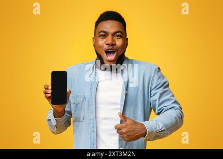 Surprised african man holding smartphone and showing thumb up Stock Photo