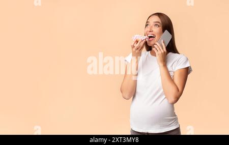 Pregnant Lady Eating Donut Chatting On Mobile Phone, Studio Shot Stock Photo