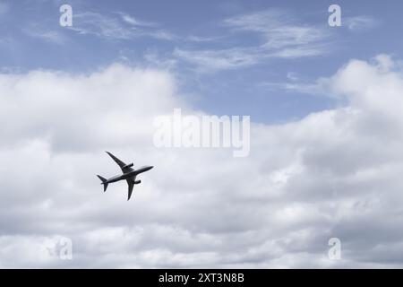 twin engined airliner flying overhead after takeoff and appearing to pass from cloudy area into blue sky Stock Photo