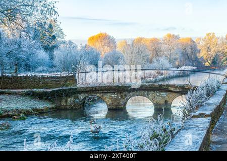 The old stone bridge over the River Coln and hoar frost on Rack Isle at sunset in the Cotswold village of Bibury, Gloucestershire, England UK Stock Photo