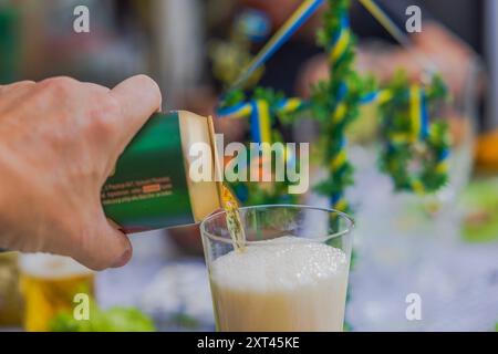 Close-up of a man’s hand pouring beer from a can into a glass at a celebratory table. Stock Photo