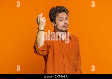 Knock-knock who is there. Confused excited Caucasian man knocking door gesture asking who is at home feeling embarrassed, no idea, being clueless and uncertain. Young guy isolated on orange background Stock Photo