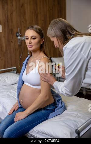 Doctor in sterile gloves making an injection to the arm of a pregnant woman Stock Photo