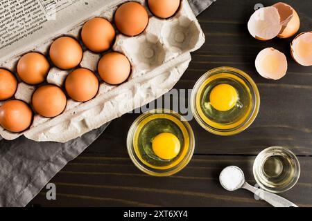 Cracked Eggs in Small Glass Bowls: Dishes with cracked eggs next to a paper egg carton and broken brown egg shells Stock Photo