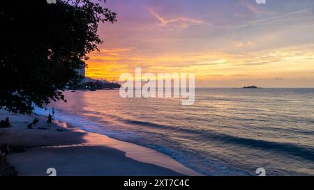 A view along Tanjing Tokong beach in Penang, Malaysia at sunset with the sun reflecting orange in the sea. Stock Photo