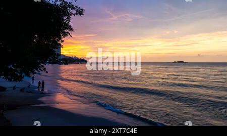 A view along Tanjing Tokong beach in Penang, Malaysia at sunset with the sun reflecting orange in the sea. Stock Photo