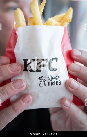 Hands holding French Fries in paper bag of KFC. Salty fries in a paper bag close up top view. KFC fast food fries. Fast food and junk food concept. Ti Stock Photo