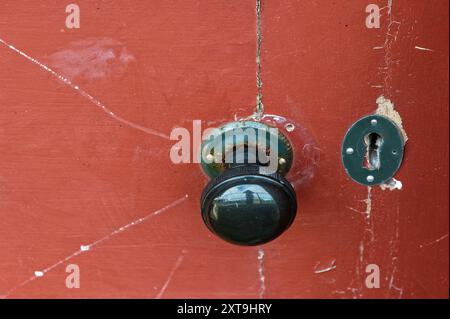 A round door handle and key hold are on a door that has seen better days. Stock Photo