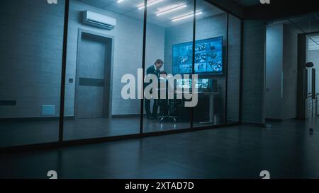 Female security worker have discussion with colleague in monitoring center, then leaves the office. African American CCTV operator works on computer with screens showing surveillance cameras footage. Stock Photo