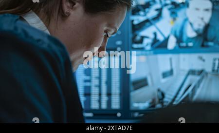 Multiethnic surveillance operators control security cameras on screens in monitoring center. Female security worker talks with African American male colleague, uses tablet computer with CCTV footage. Stock Photo