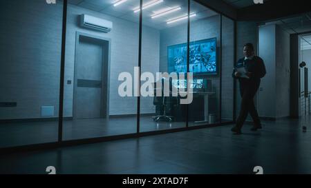 Female security worker have discussion with colleague in monitoring center, then leaves the office. African American CCTV operator works on computer with screens showing surveillance cameras footage. Stock Photo