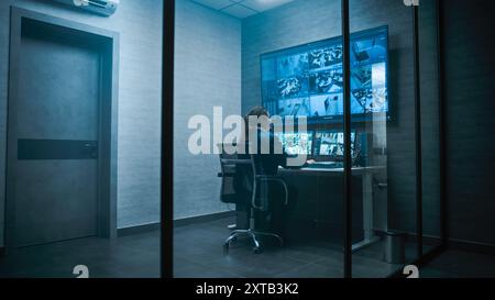 Female security worker have discussion with colleague in monitoring center, then leaves the office. African American CCTV operator works on computer with screens showing surveillance cameras footage. Stock Photo