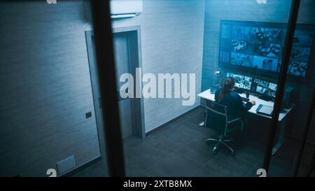 Female CCTV operator controls security cameras in monitoring center on computer. Surveillance video footage displayed on multiple monitors and big digital screen. Stock Photo