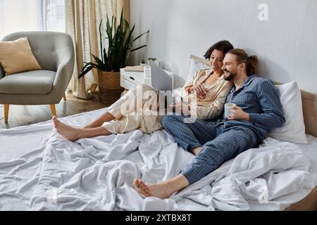 A couple relaxes in bed, watching something on a laptop. Stock Photo