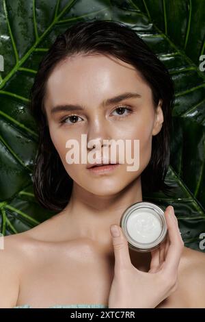 A woman with clear skin holds a cream jar in front of lush green foliage. Stock Photo