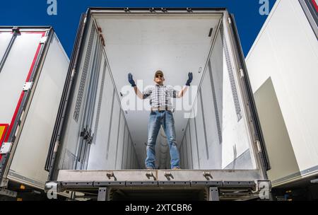 A warehouse worker stands confidently inside an empty semi trailer, directing operations. Truck transportation job. Stock Photo