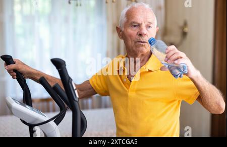 Senior man using elliptical trainer and drinking water Stock Photo