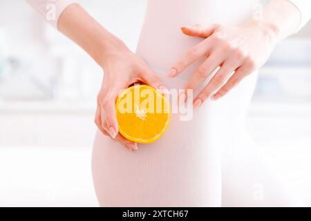 A woman is holding an orange in her hand. The orange is cut in half and placed on her thigh Stock Photo