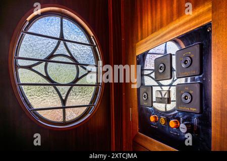 A round porthole window with a floral glass pattern and a switch panel with brass knobs for the train and carriage lighting decorate the door of a carriage in the Alpine Classic Pullman Express. The train dates from 1931 and originally ran as the 'Golden Mountain Pullman Express' on the Montreux–Bernese Oberland railway line. The Rhaetian Railway bought it in 1939 and used it for army inspection trips from 1940 until the end of the war. The Verein Pro Salonwagen, founded in 1998, rescued the train, which today stands as a protected historic rail monument in the canton of Graubünden. Reichenaue Stock Photo