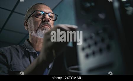 Close up of mature specialist inserting cable into server rack. Network administrator works in server room using tablet computer. Operation of information systems and networks. Data storage center. Stock Photo