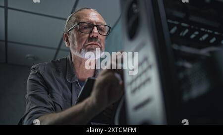 Close up of male system administrator setting up network equipment using tablet computer. Mature technician works in server room. Local area network and web servers maintenance. Data storage center. Stock Photo