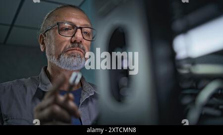 Close up of male system administrator setting up network equipment using tablet computer. Mature technician works in server room. Local area network and web servers maintenance. Data storage center. Stock Photo