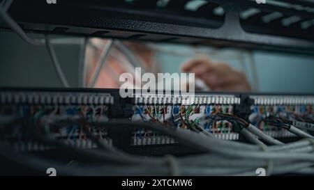 Male system administrator connects cables with server rack working in server room. Maintenance of local area network or web servers. Operation of information systems and networks. Data storage center. Stock Photo