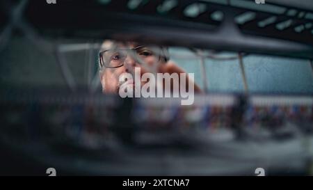 Male system administrator connects cables with server rack working in server room. Maintenance of local area network or web servers. Operation of information systems and networks. Data storage center. Stock Photo