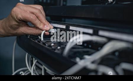 Male system administrator connects cables with server rack working in server room. Maintenance of local area network or web servers. Operation of information systems and networks. Data storage center. Stock Photo