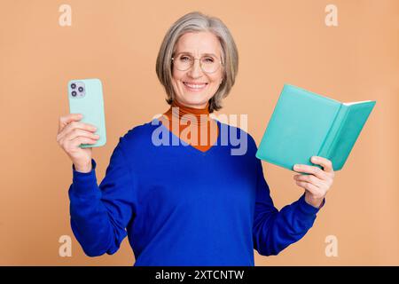 Photo portrait of nice senior woman reading book hold device wear trendy blue outfit isolated on beige color background Stock Photo